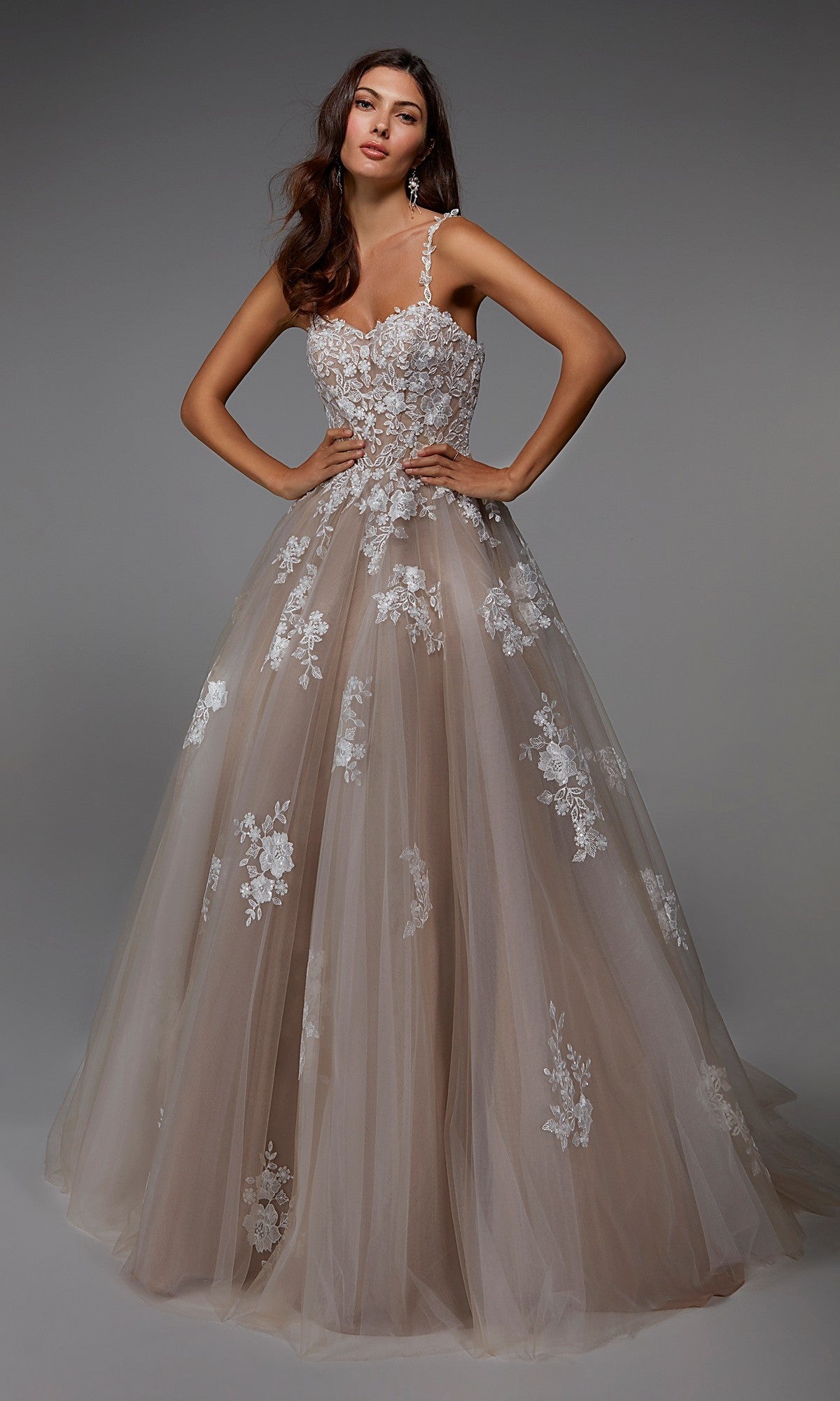 A woman wearing the Alyce 7043 long formal dress in Ivory/Latte, featuring a sleeveless lace bodice and a full tulle ballgown skirt, stands against a plain gray background.